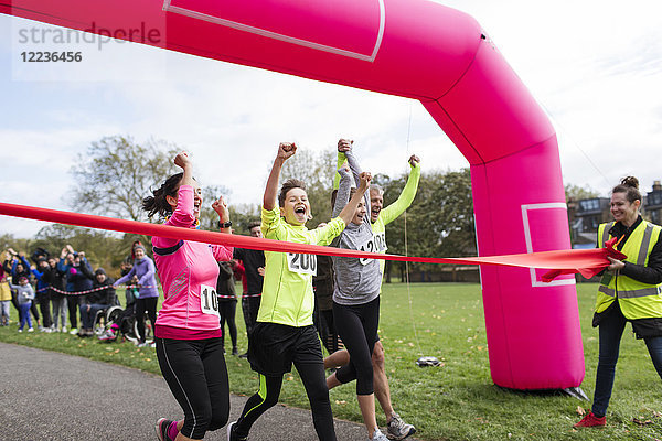 Enthusiastische Familienläufer überqueren die Ziellinie des Charity-Laufs im Park