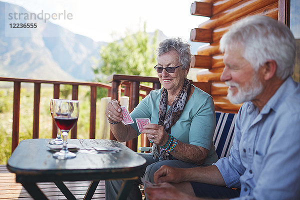 Aktives Seniorenpaar trinkt Wein und Spielkarten auf dem Hüttenbalkon