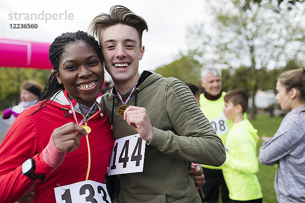 Portrait lächelndes  selbstbewusstes Paar mit Medaillen beim Benefizlauf im Park