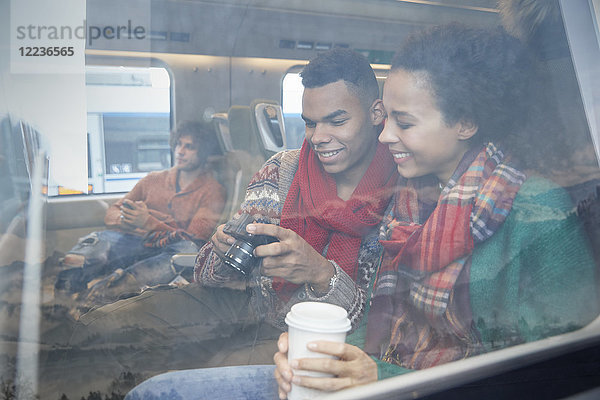 Junges Paar mit Kaffee beim Blick auf die Digitalkamera am Fenster des Personenzuges