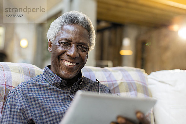 Portrait lächelnder  selbstbewusster Senior mit digitalem Tablett auf dem Sofa