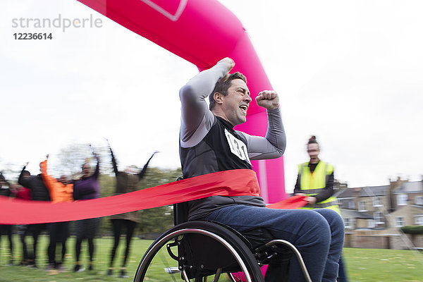 Enthusiastischer Mann im Rollstuhl überquert die Ziellinie  jubelt beim Charity-Rennen im Park.