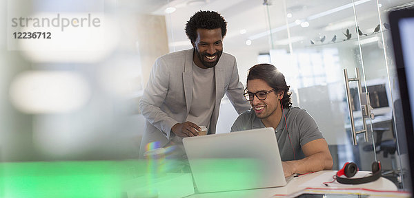Lächelnde kreative Geschäftsleute arbeiten am Laptop im Büro