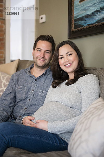 Mid adult couple sitting on sofa and smiling to camera