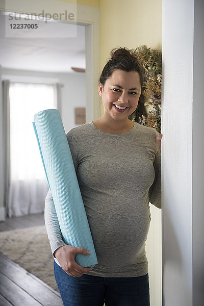 Schwangere Frau steht in der Tür und hält eine Gymnastikmatte