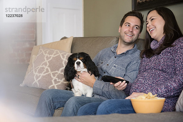 Glückliches mittleres erwachsenes Paar entspannt sich auf Sofa mit Hund