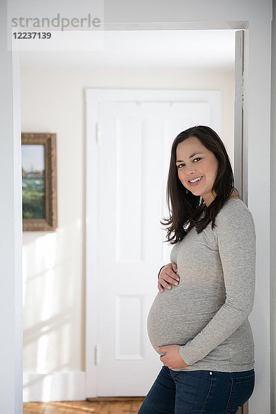 Porträt einer schwangeren Frau  die in der Tür steht und ihren Bauch berührt