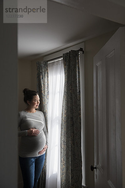 Schwangere Frau schaut durch ein Fenster