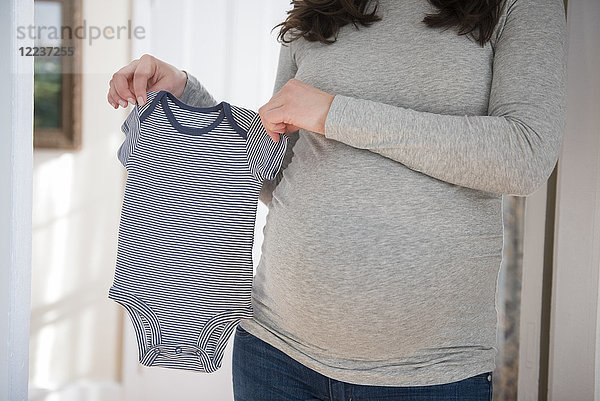 Schwangere Frau hält Säuglingsbodysuit