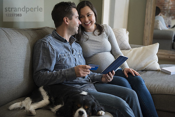 Mid adult couple shopping online in living room  sitting on sofa with puppy