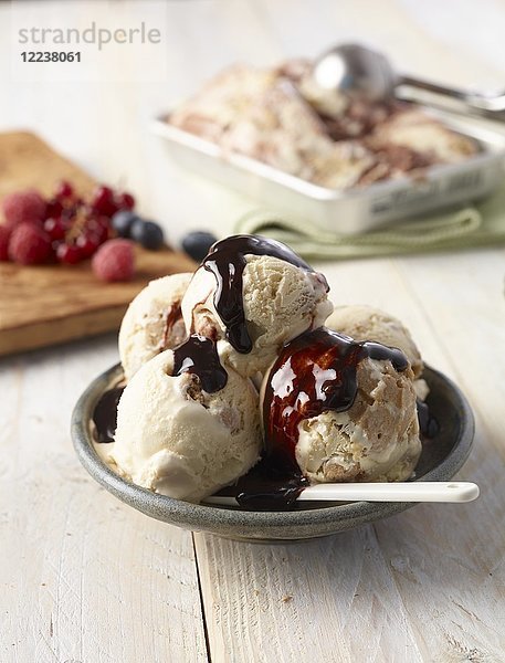 Eis mit Schokoladensauce  mit frischen Beeren im Hintergrund