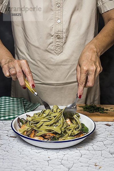 Eine Frau serviert grüne Tagliatelle mit Meeresfrüchten