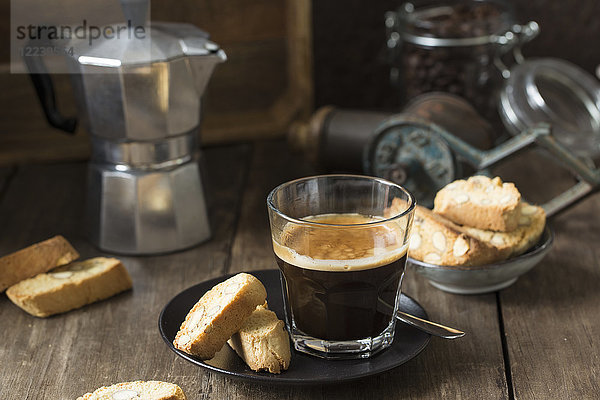 Espresso im Glas und Cantuccini mit einer Kaffeemaschine auf dem Herd im Hintergrund