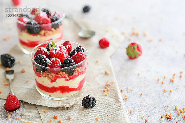 Geschichtete Desserts in Gläsern mit Puddingcreme  Fruchtsauce  Kekskrümeln und Beeren