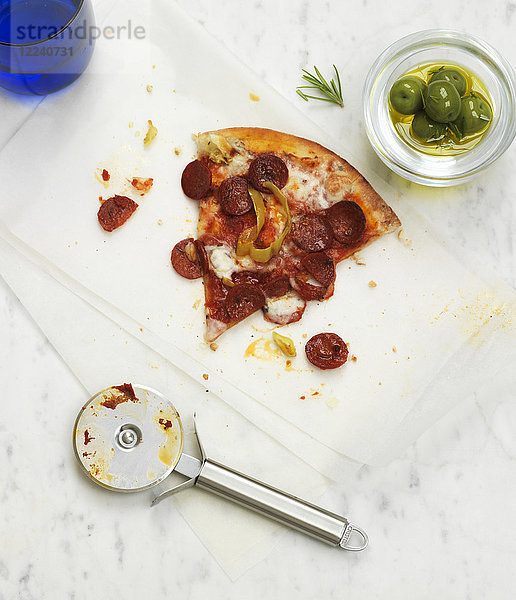 Ein Stück Peperoni-Pizza mit einer Schale grüner Oliven
