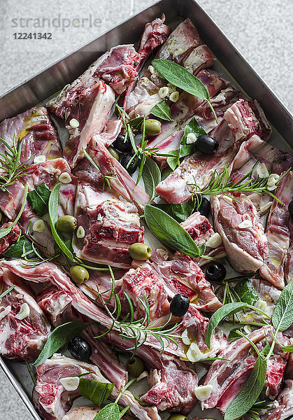 Rohe Lammfleischstücke mit Knoblauch  Oliven  Salbei  Rosmarin und Lorbeerblättern auf einem Backblech
