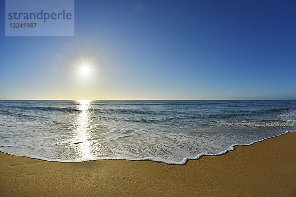 Die Brandung bricht sich an der Küste des Ninety Mile Beach am Paradise Beach  während die Sonne über dem Meer in Victoria  Australien  scheint.