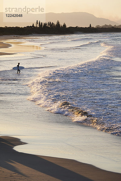 Silhouette eines Surfers  der die Wellen beobachtet  die am Strand von Byron Bay in New South Wales  Australien  ans Ufer schlagen