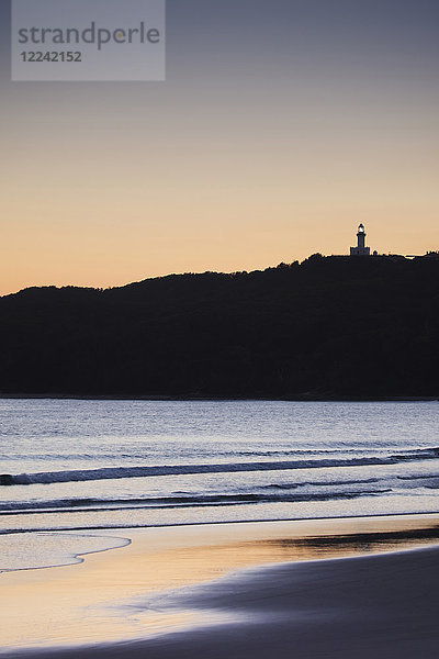 Silhouette des Leuchtturms von Cape Byron auf einer Bergkuppe und Strand bei Sonnenuntergang in Byron Bay in New South Wales  Australien