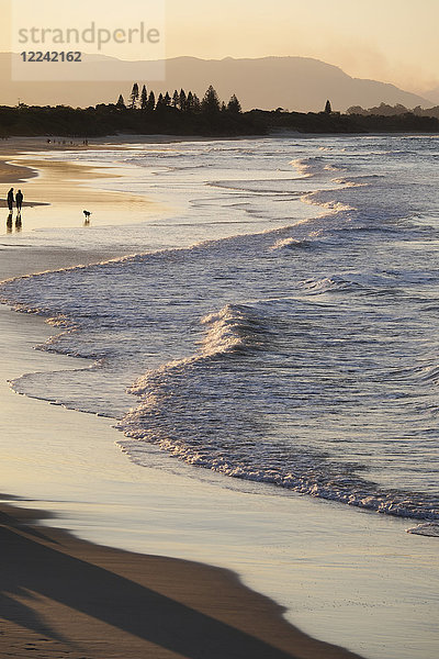 Silhouette von Menschen  die am Strand spazieren gehen  während pastellfarbene Wellen an die Küste von Byron Bay in New South Wales  Australien  schlagen