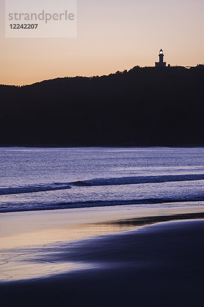 Silhouette des Leuchtturms von Cape Byron auf einer Bergkuppe und Strand bei Sonnenuntergang in Byron Bay in New South Wales  Australien