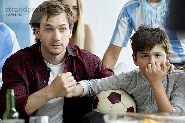 Vater und Sohn halten sich an den Händen  während sie das Fußballspiel zu Hause sehen.