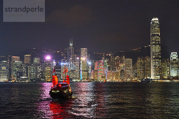 Traditionelle Dschunke auf dem Victoria Harbour mit beleuchteter Stadtsilhouette bei Nacht  Hongkong  China  Asien