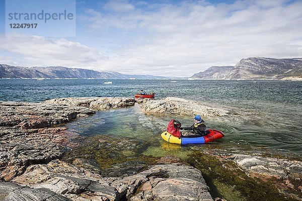 Zwei Personen mit Packwagen auf Fjord  Felsen  hinter Bergen  Grönland  Nordamerika