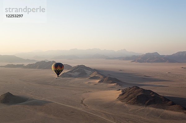 Heißluftballon über einer trockenen Ebene und isolierten Gebirgskämmen  in der Morgendämmerung  Namib-Wüste  Luftaufnahme aus einem zweiten Ballon  NamibRand Nature Reserve  Namibia  Afrika