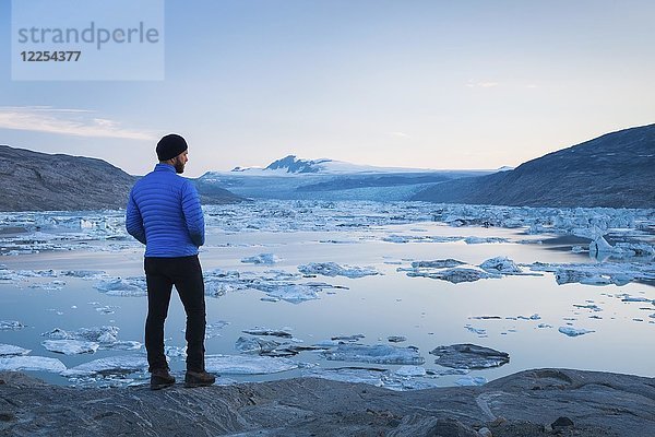 Mann steht auf Felsen mit Blick auf einen Gletschersee mit kleinen Eisbergen  Grönland  Nordamerika