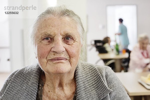 Demente Seniorin in einem Altenheim  unscharfes Pflegepersonal im Rücken  Deutschland  Europa