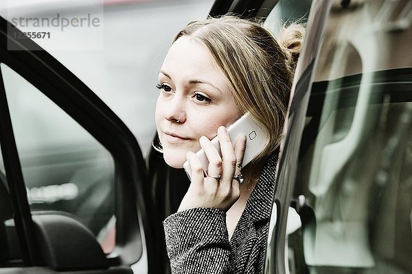 Junge Frau sitzt an einer offenen Tür mit ihrem Smartphone im Auto  Deutschland  Europa
