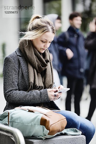 Junge Frau  Studentin  sitzt auf dem Campus mit ihrem Smartphone  Köln  Nordrhein-Westfalen  Deutschland  Europa