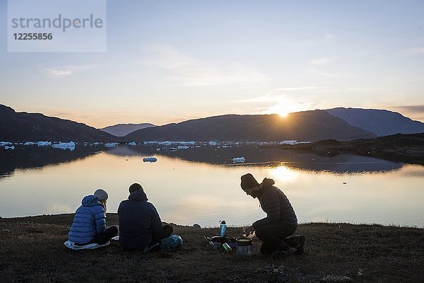 Trekkinggruppe am Fjordsee in bergiger Landschaft bei der Essenszubereitung  Abendstimmung  Westgrönland  Grönland  Nordamerika