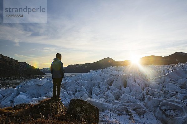 Mann steht bei Sonnenuntergang auf einem zerfurchten Gletscher  Westgrönland  Grönland  Nordamerika