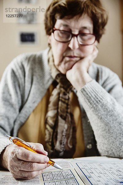 Senior sitzt am Tisch zu Hause und löst Rätsel  Sudoku  Kreuzworträtsel  Köln  Nordrhein-Westfalen  Deutschland  Europa