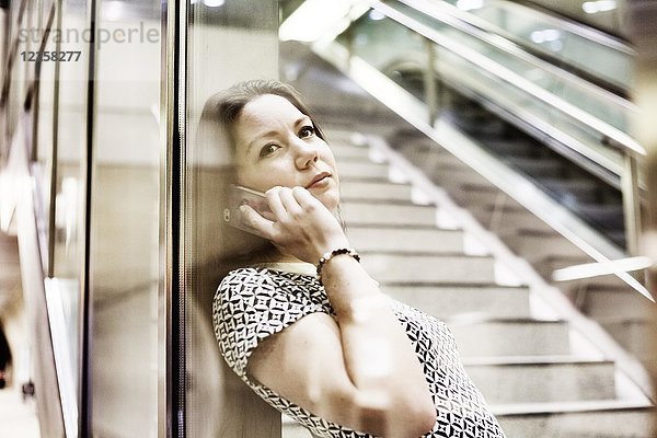 Junge Frau posiert mit Smartphone hinter einer Glaswand in einer U-Bahn-Station  Köln  Nordrhein-Westfalen  Deutschland  Europa