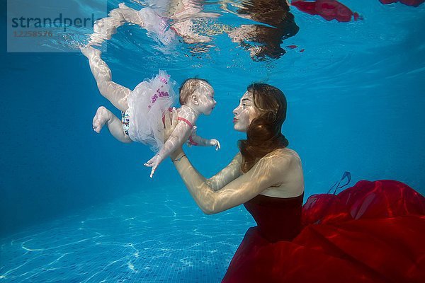 Schöne junge Frau im roten Kleid mit Baby posiert unter Wasser im Pool  Ukraine  Europa