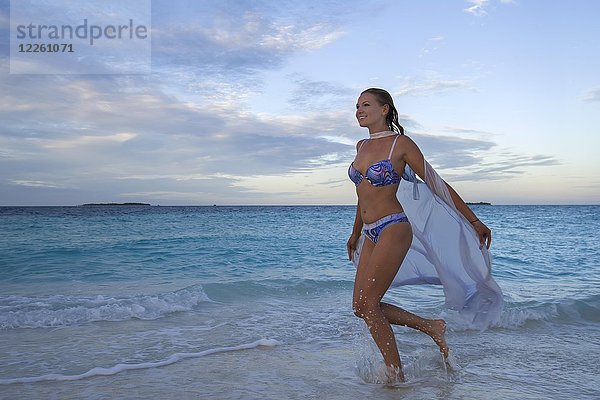 Junge Frau im Bikini läuft am Strand in der Abenddämmerung  Insel Fuvahmulah  Indischer Ozean  Malediven  Asien