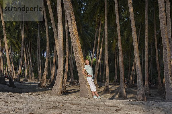 Junge schöne Frau lehnt an einer Palme in einem tropischen Wald am Strand  Fuvahmulah Island  Indischer Ozean  Malediven  Asien