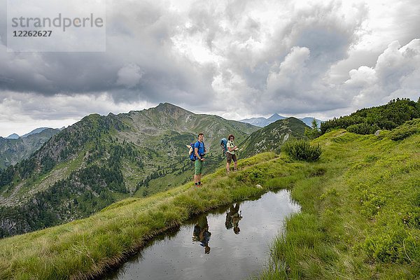 Wanderer spiegeln sich in einem kleinen See  Schladminger Höhenweg  Schladminger Tauern  Schladming  Steiermark  Österreich.