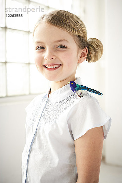 Porträt eines glücklichen kleinen Mädchens mit Spielzeugvogel auf der Schulter