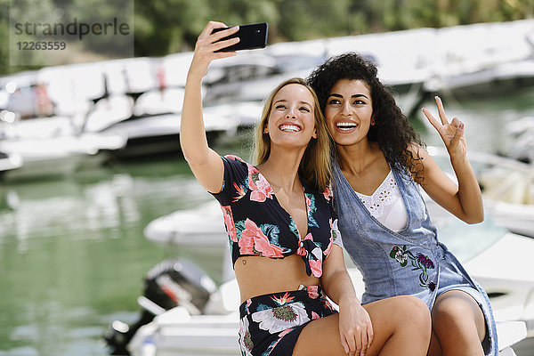 Zwei glückliche junge Frauen  die im Sommer einen Selfie am Yachthafen machen.