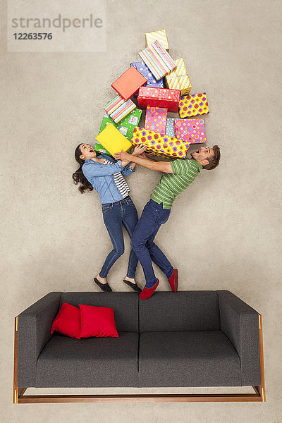 Ein Paar steht auf der Couch und hält einen großen Stapel Geschenke.