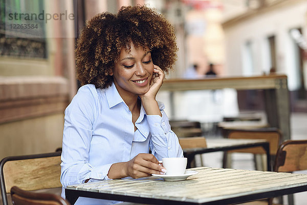 Lächelnde Frau mit Afro-Frisur sitzend im Outdoor-Café
