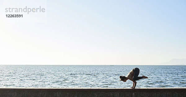 Junge Frau beim Yoga an einer Wand am Meer