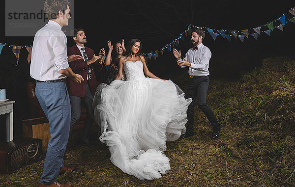 Fröhliche Braut beim Tanzen und Spaß haben  während ihre Freunde auf einer Nachtfeld-Party klatschen.