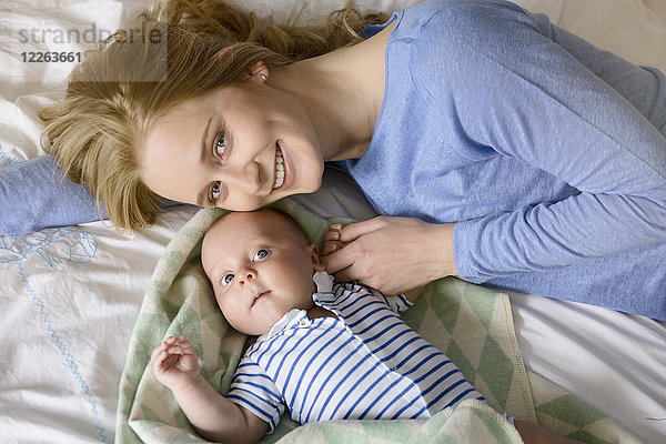 Porträt der lächelnden Mutter mit ihrem kleinen Jungen auf dem Bett liegend