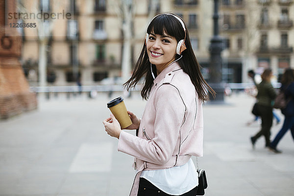 Spanien  Barcelona  lächelnde Frau mit Kaffee und Kopfhörer in der Stadt