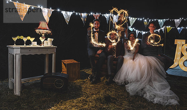 Hochzeitspaar und Freunde  die das Wort Liebe mit Wunderkerzen auf einer Nachtparty im Freien machen.